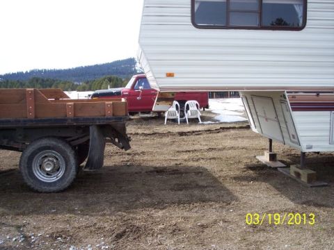 1973 Ford F-250 - A red pickup truck is parked with a camper, with a flatbed trailer in front of it.