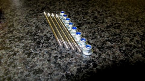 1996 Ford Bronco - A set of threaded studs and matching nuts are laid out on a dark, speckled surface.