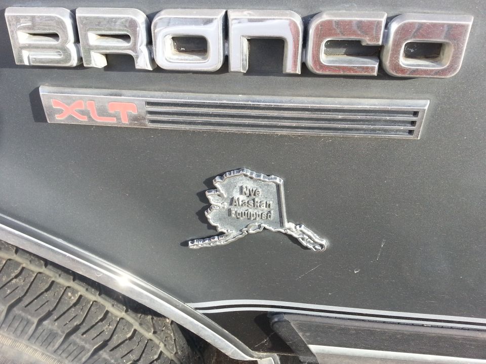Close-up of 'BRONCO' and 'XLT' badges on a vehicle, with an Alaska-shaped emblem that says 'Nye Alaskan Equipped'