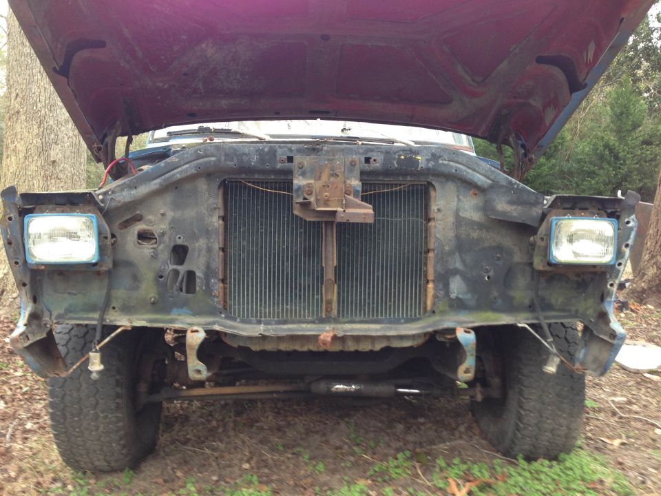 front of a truck with hood open, missing grille and headlights