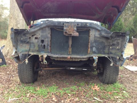 1979 Ford Bronco - The front end of a vehicle is visible with its hood open, revealing a damaged and incomplete grille area.