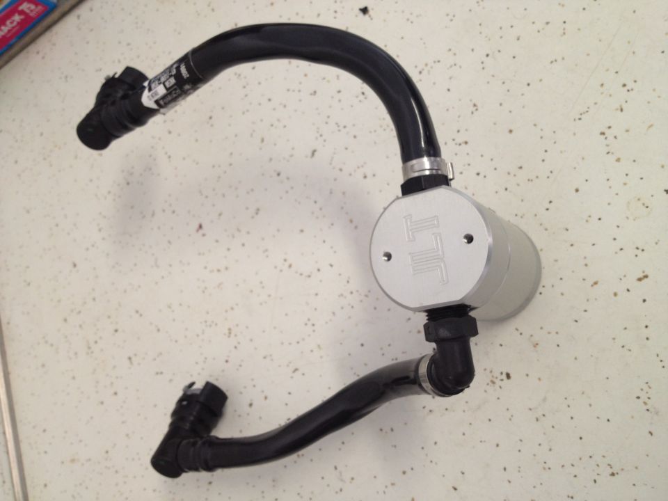 oil catch can with black hoses attached, silver canister has 'JLT' logo
