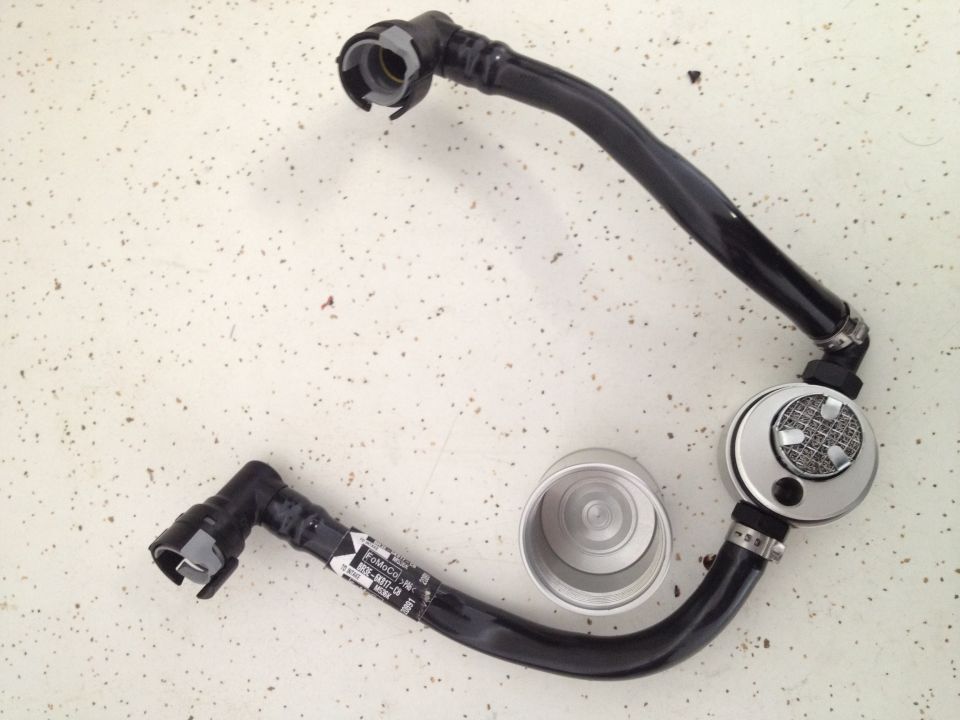 Automotive fuel line with a silver canister and black hoses, laid out on a speckled surface