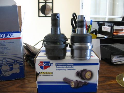 1995 Ford Bronco - Two Moog ball joints stood upright on a CarQuest "Suspension & Steering" box on a wood desk, one black-coated and one bare steel, threaded…