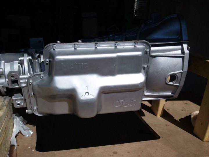 Transmission pan with Ford logo and 'Metra' text. It's silver and bolted to a transmission