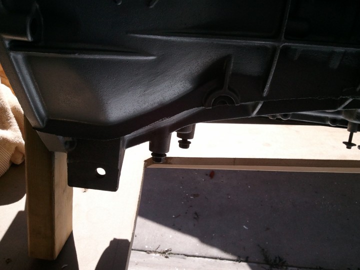 Black transmission housing on wooden supports, showing mounting brackets and bolts