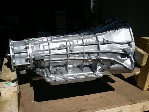1994 Ford Bronco - A silver transmission part is shown resting on a wooden surface, with a watermark for Supermotors.net at the bottom right.