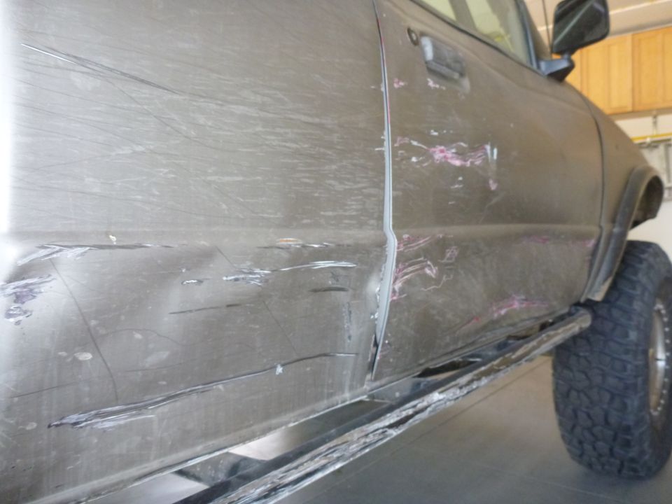 Damaged gray truck side panel and door with dents and scratches