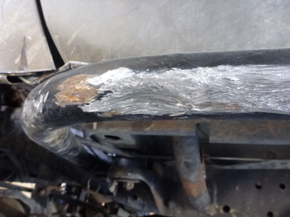 Close-up of a bent and scraped black metal tube with rust and white paint marks, showing undercarriage components
