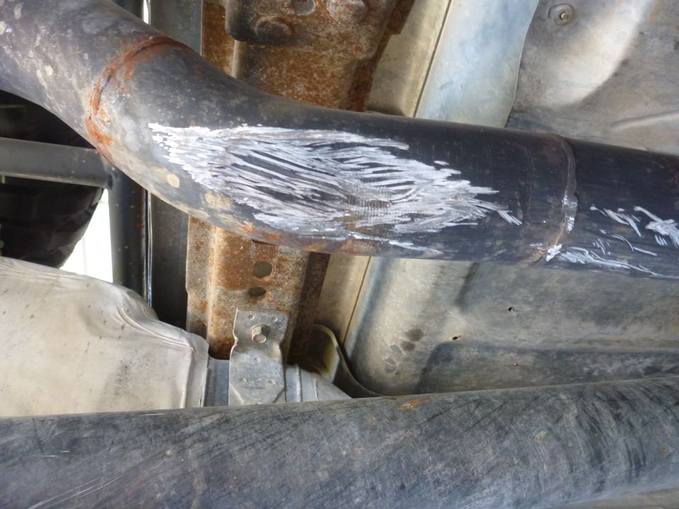 Undercarriage of a vehicle showing a scraped exhaust pipe with white paint marks and rusty metal components