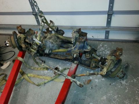 1987 Toyota 4Runner - Front axle assembly, likely from an older SUV, is suspended by chains and resting on a red stand.