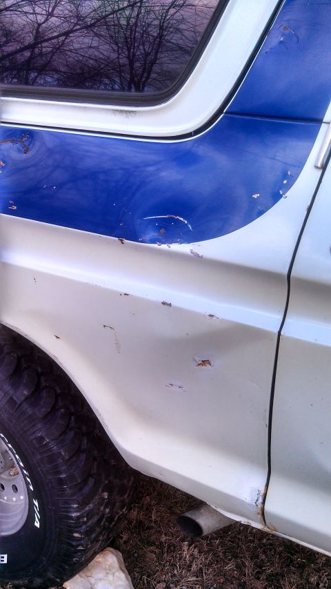 1979 Ford Bronco - The side of a vintage Ford Bronco shows wear and tear with visible rust and a dent on the body panel.