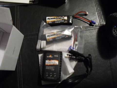 1986 Ford Bronco - A collection of RC car batteries and a charger are laid out on a textured surface.