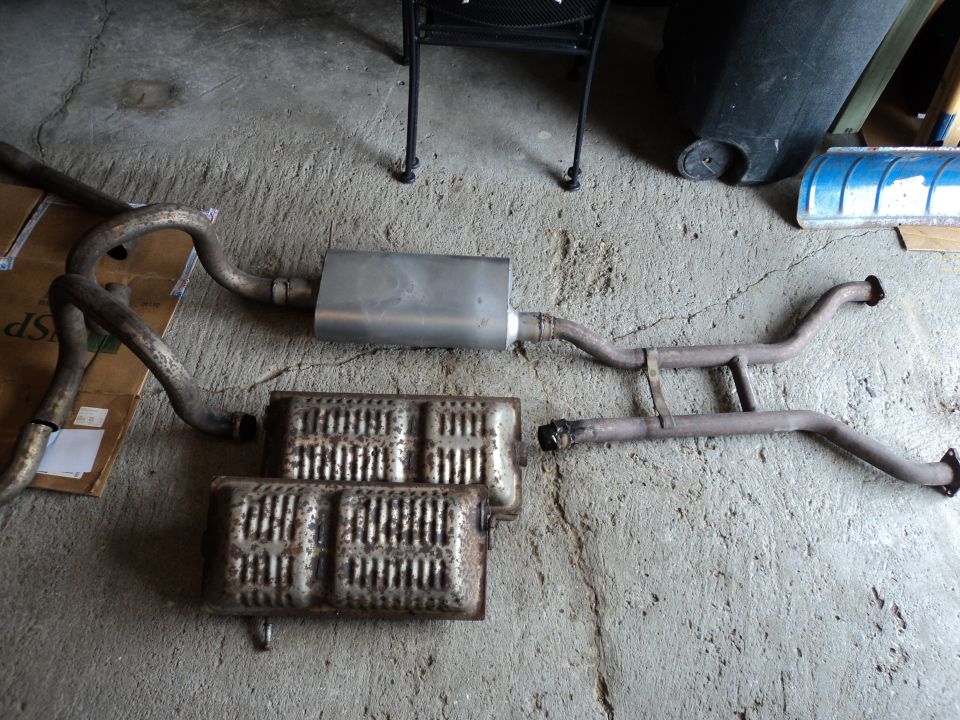 Exhaust system components laid out on a concrete floor. Includes mufflers and pipes