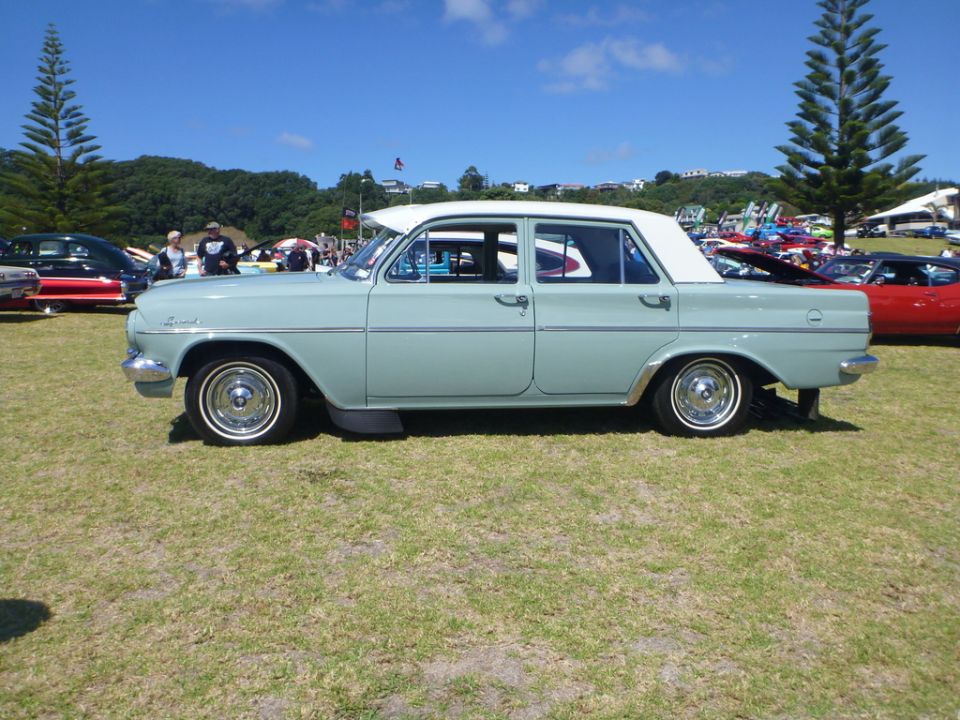 Pale blue sedan with white roof parked on grass, other cars and trees in background
