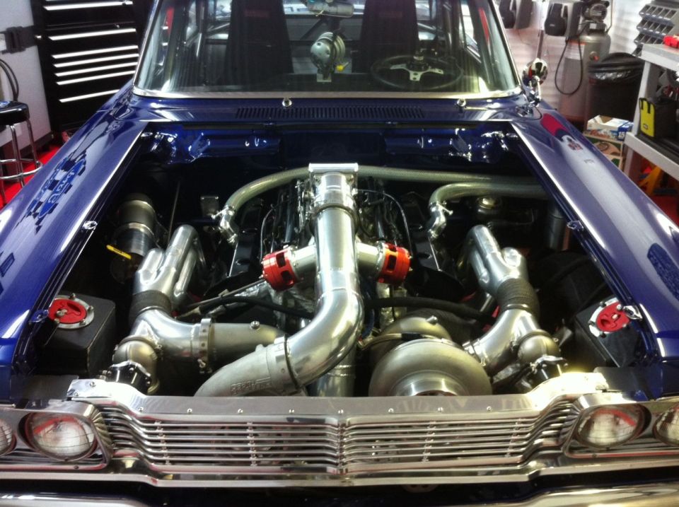 Custom twin-turbo V8 engine in a blue car, hood open, showing intercooler piping and turbos