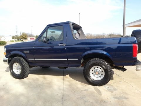 1995 Ford Bronco - This dark blue Ford Bronco features a removable top and is shown from the side with off-road tires.