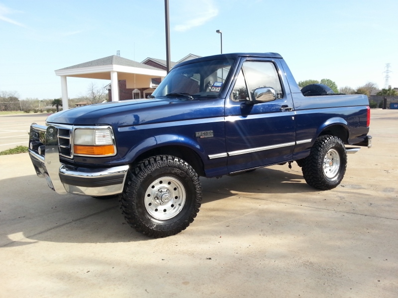 Blue 1995 Ford Bronco with aftermarket chrome bull bar and off-road tires