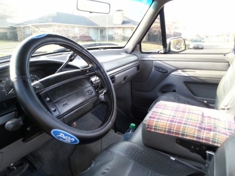 1995 Ford Bronco - The interior of a Ford truck from the early 1990s is visible, with a plaid-covered armrest and a Ford logo on the steering wheel.