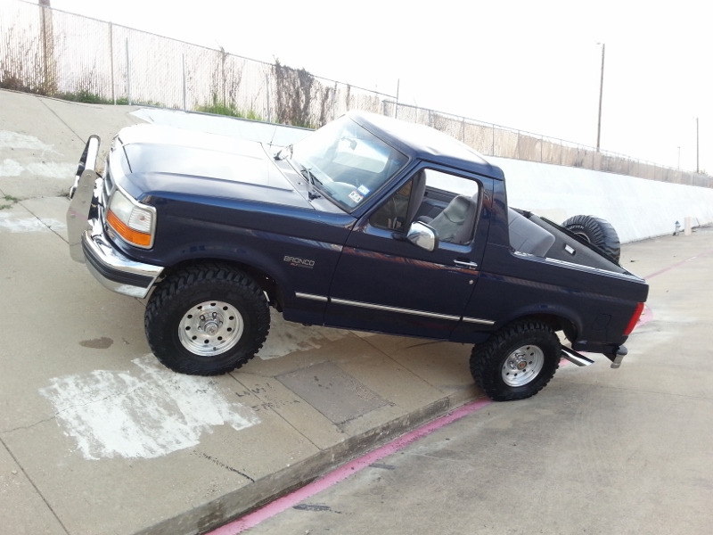 Dark blue Ford Bronco parked on a concrete incline, spare tire mounted on the back