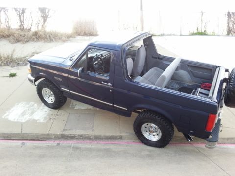 1995 Ford Bronco - This dark blue convertible SUV, likely from the early 1990s, is parked on a sidewalk.