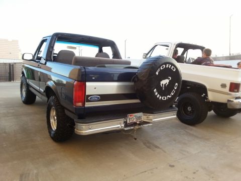 1995 Ford Bronco - A dark blue Ford Bronco is parked next to a white pickup truck, both with their tops removed.