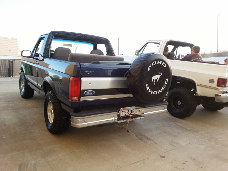 Dark blue Ford Bronco with spare tire cover, parked next to a white pickup truck