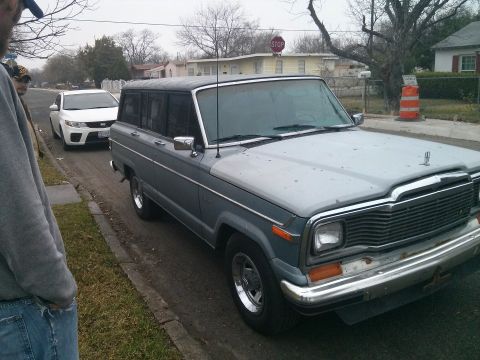 1982 Jeep Wagoneer - A gray Jeep Wagoneer is parked on the side of the road, with a white car behind it.
