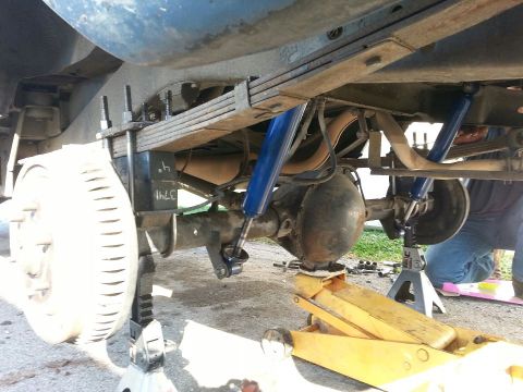 1982 Jeep Wagoneer - Close-up view of the rear axle and suspension system, showing leaf springs and blue shock absorbers. Some text is visible on a component.