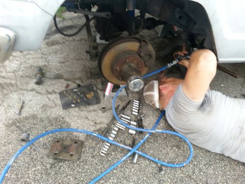 1982 Jeep Wagoneer - Mechanic performs maintenance on the front wheel hub of a white 1982 Jeep Wagoneer.