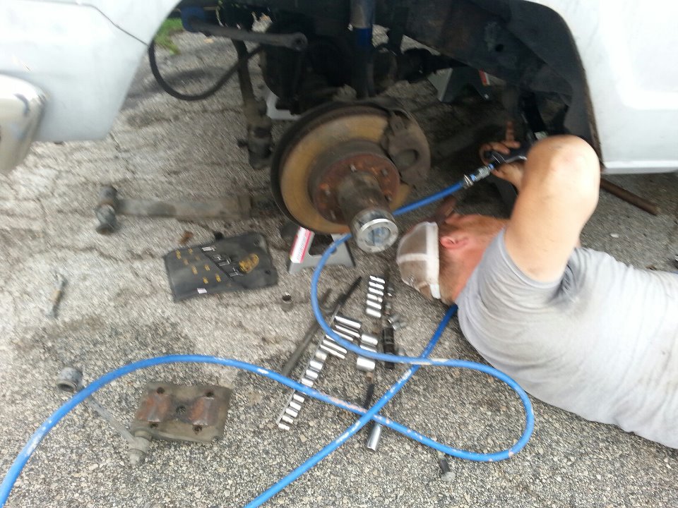 White 1982 Jeep Wagoneer front wheel hub and brake assembly with mechanic working on it