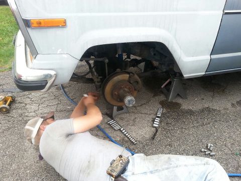 1982 Jeep Wagoneer - Mechanic works on the front wheel assembly of a 1982 Jeep Wagoneer, which is raised on jack stands.