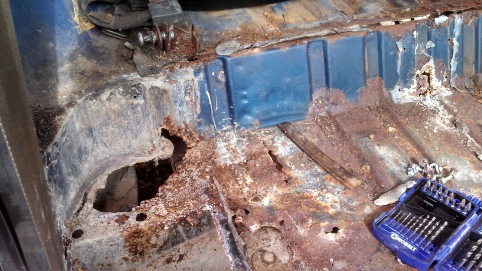 Blue interior floor pan with extensive rust damage and holes, showing structural deterioration