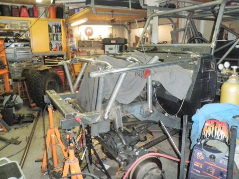 1961 International Scout 800 - A custom off-road vehicle chassis is under construction in a cluttered garage, surrounded by tools and welding equipment.