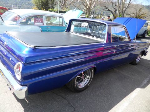 1973 Ford Ranchero - A blue pickup truck is parked next to a light blue sedan with a 'For Sale' sign in the window.