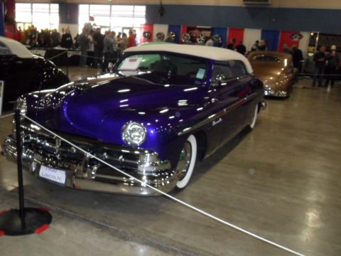1973 Ford Ranchero - A custom purple 1950 Lincoln convertible is displayed indoors, with other vehicles and people in the background.