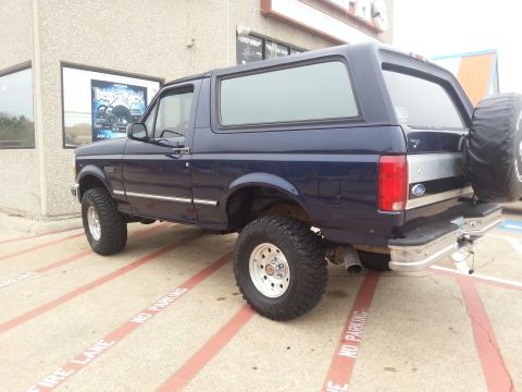 1995 Ford Bronco - 1995 Ford Bronco parked on pavement with red lines, spare tire mounted on the rear.