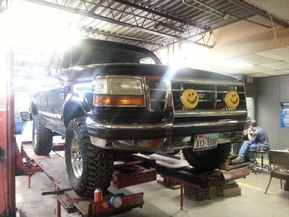 Black 1995 Ford Bronco on a lift, front view, with smiley face lights on the grille