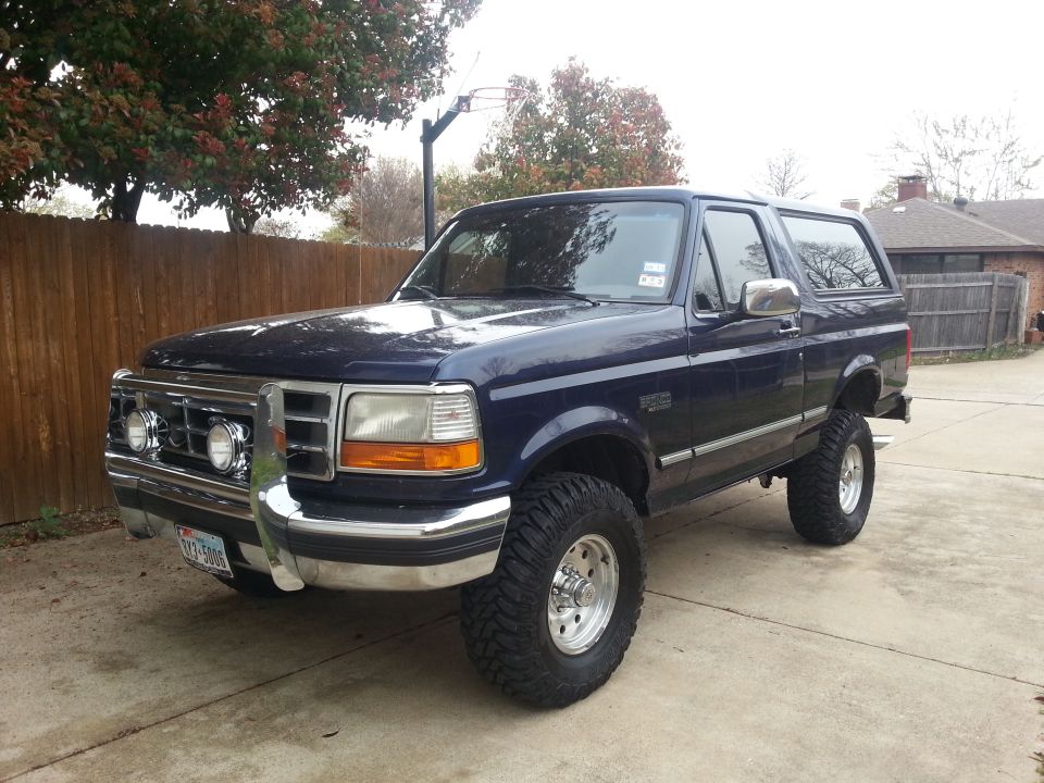 Dark blue Ford Bronco parked on a driveway. It has aftermarket wheels and tires