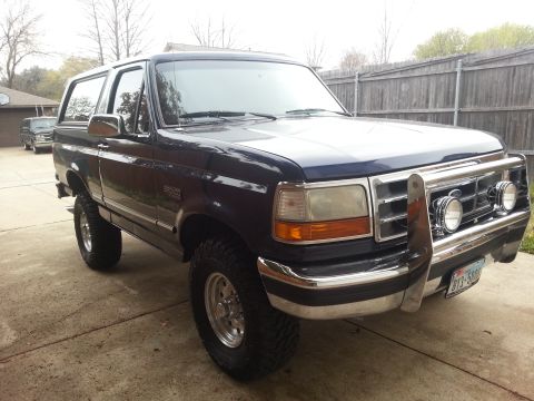 1995 Ford Bronco - A dark blue Ford Bronco is parked in a driveway with another vehicle in the background.