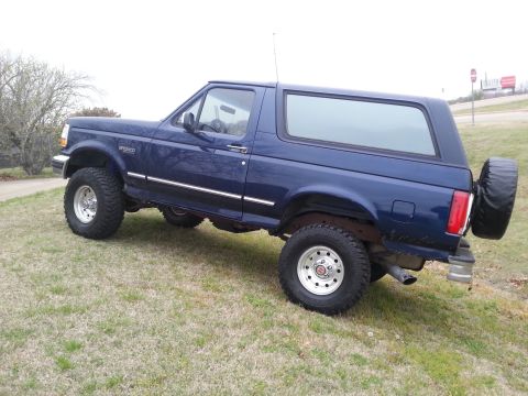 1995 Ford Bronco - This blue Ford Bronco is shown from a 3/4 front angle on a grassy incline.