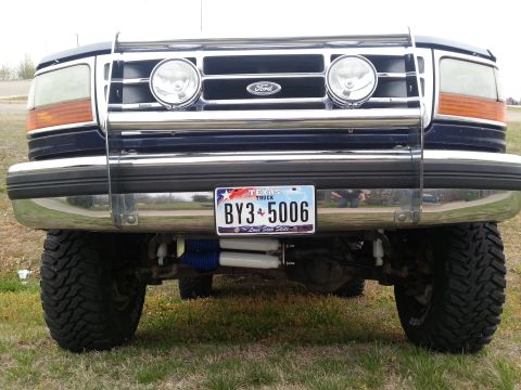 1995 Ford Bronco - Frontal view of a blue Ford Bronco with a chrome grille guard and aftermarket shocks.