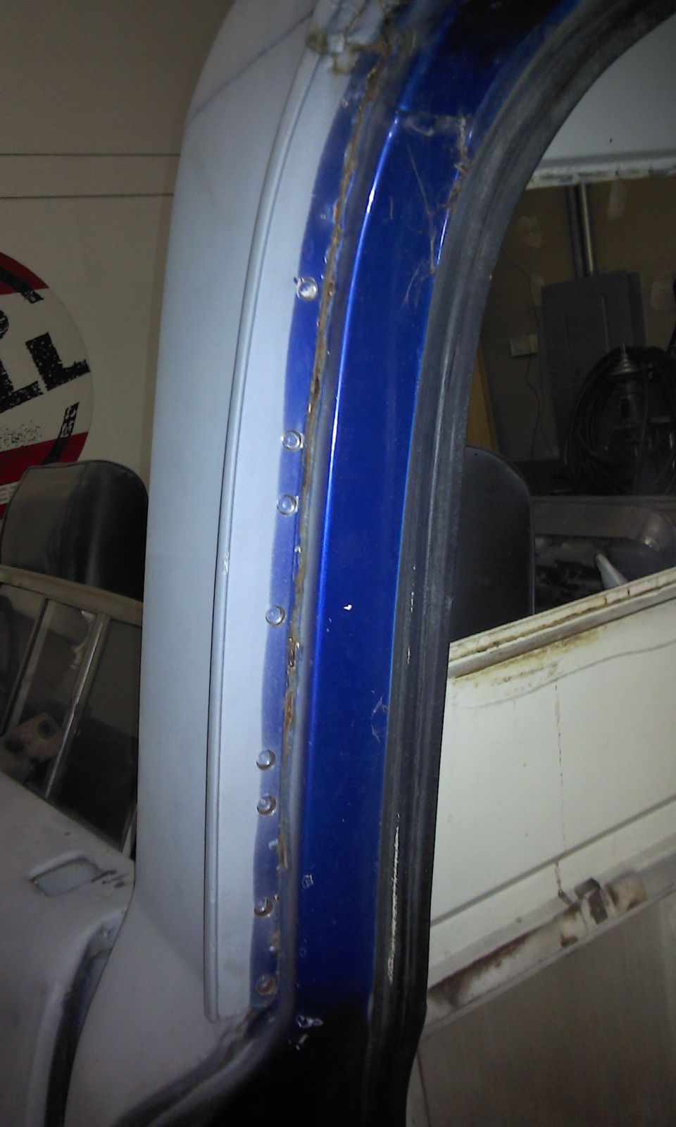 Close-up of a truck's blue door frame with visible rivets and some rust