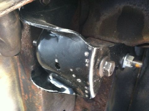 1996 Ford Bronco - Close-up of a vehicle's undercarriage shows a black metal spring hanger bracket with visible bolts and surrounding rust.