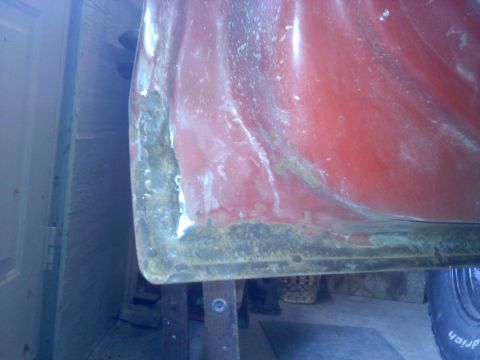 1978 Ford Bronco - The lower edge of a red vehicle's body panel exhibits significant rust and wear.