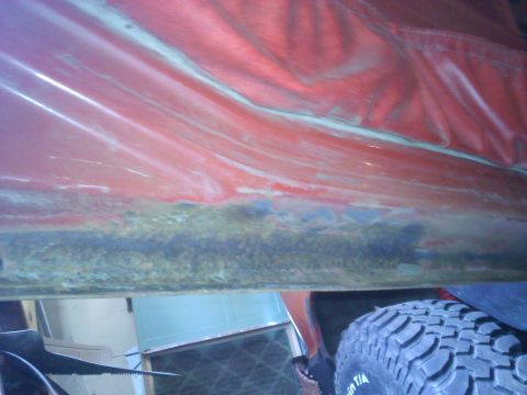 1978 Ford Bronco - Close-up of a red vehicle's interior panel showing rust and damage, with a tire visible.