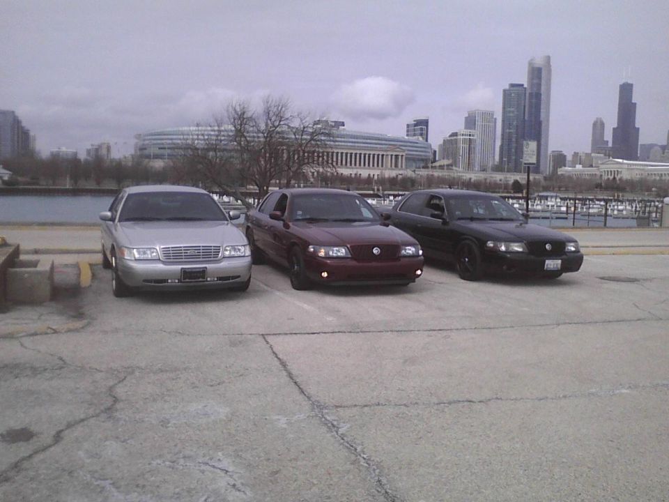 Three sedans parked in a lot with a city skyline in the background