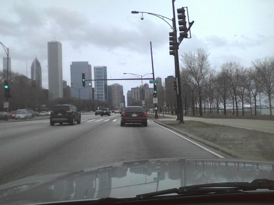 Rear view of a dark sedan on a city street with skyscrapers in the background