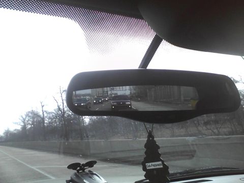 2003 Ford Crown Victoria - Multiple vehicles are seen on the highway through the rearview mirror, with an air freshener hanging from it.