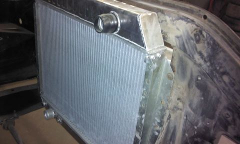 1967 Ford F-100 - Aftermarket aluminum radiator installed in a vehicle's engine bay, showing the core and inlet/outlet fittings.